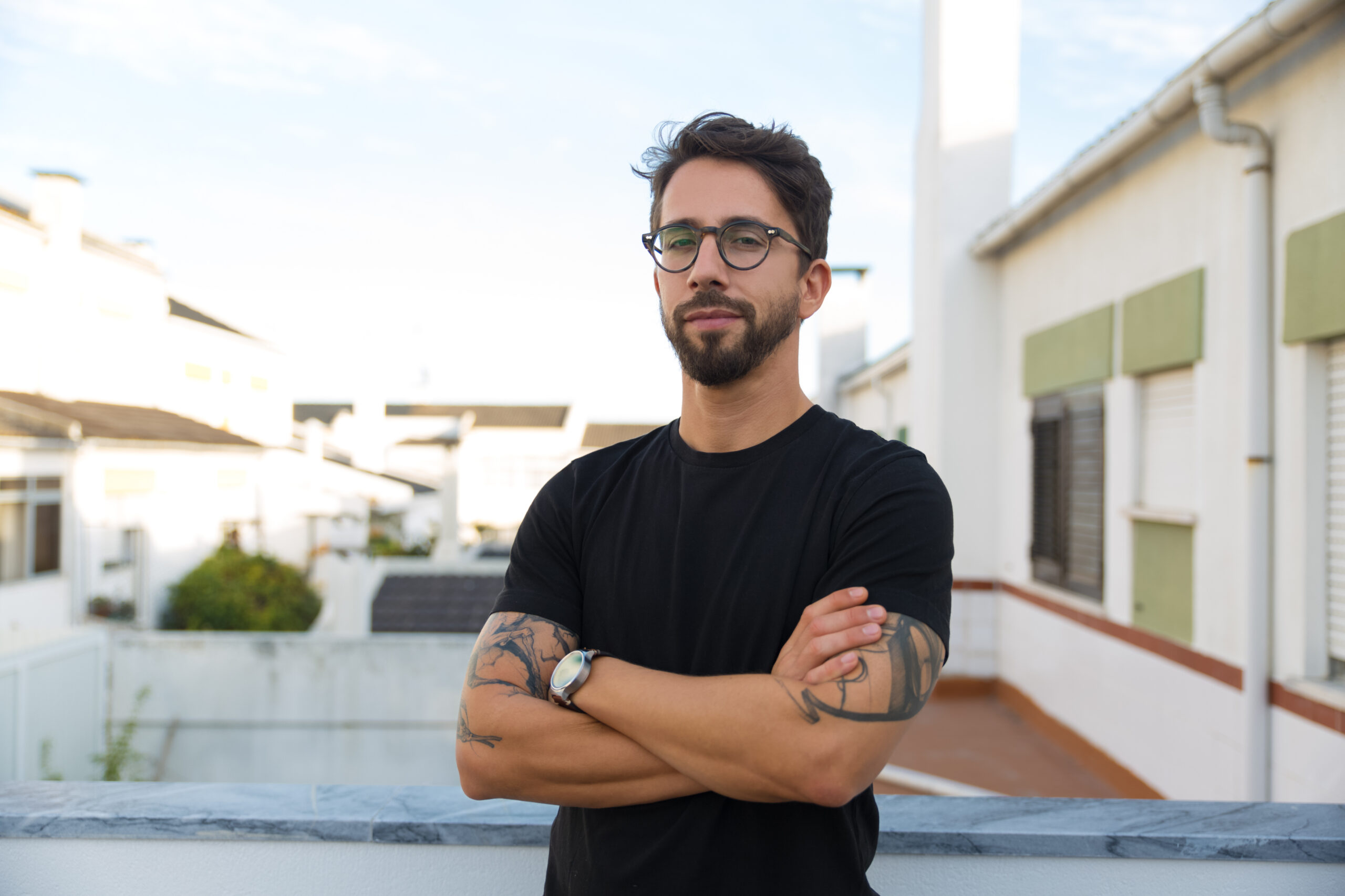 confident stylish guy with tattoos posing on apartment balcony
